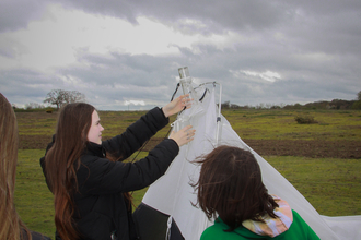 Two work experience students taking down a trap in a field with overcast skies