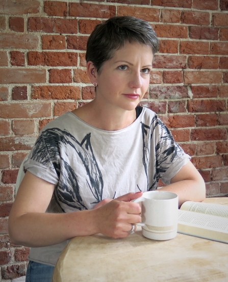 Melissa Harrison, sitting at a table with a cup of tea in front of a red brick wall
