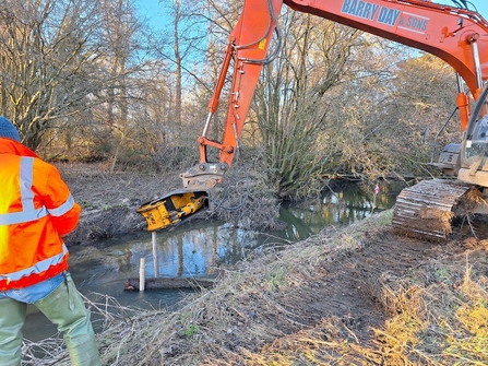 A digger placing a log flow deflector in the river channel.