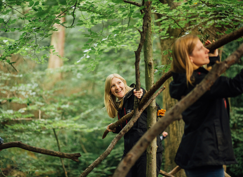 Two girls with blonde hair and black wildlife trust shirts volunteering in woodland