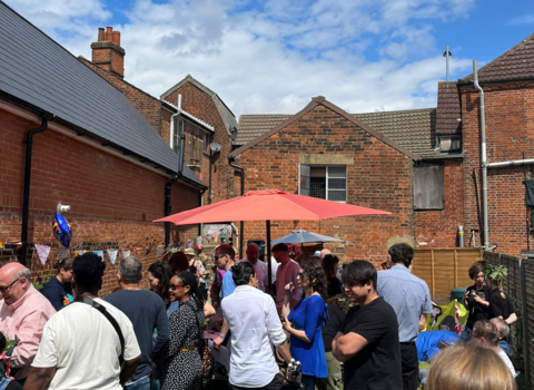 Lots of people standing in garden behind the Hive in Ipswich, under a blue sky.