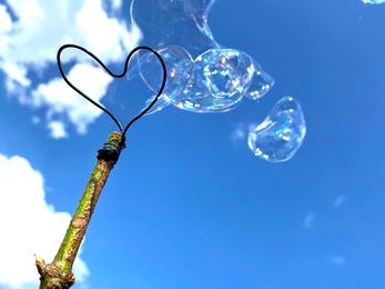 a heart-shaped bubble blowing stick made from a stick and wire against a blue sky filled with bubbles