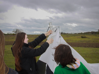 Two work experience students taking down a trap in a field with overcast skies