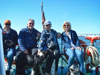 Four people and a dog sitting on a boat smiling 