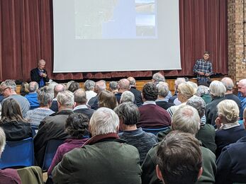 A community hall with people sat in rows listening to a talk