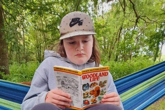 Mason reading a book about woodland wildlife in a hammock at Foxburrow Farm