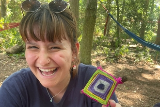 Faye in the woodland, holding up a small crafted kite, whilst sitting in the woods. 