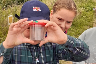 Young boy holding up a baby toad in a bug pot. 