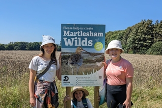 Three girls standing next to a Martlesham Wilds sign