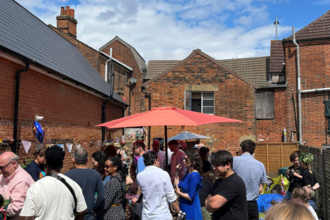 Lots of people standing in garden behind the Hive in Ipswich, under a blue sky.