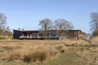A view over the fen at Carlton Marshes towards the Visitor Centre, with a family walking along a footpath.