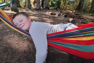 A young boy laying across a rainbow coloured hammock with a big smile