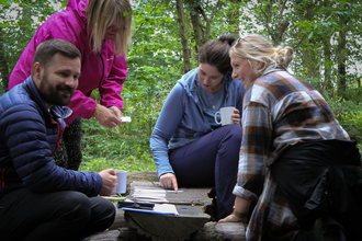 Four people gathered around a low wood table in the woods