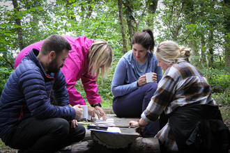 Four people huddle around a log in an ancient woodland analysing bark types.