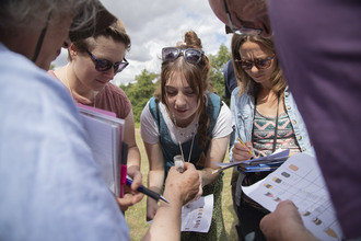People holding paper looking at an insect