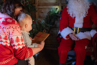 A child at Santa's grotto sitting on an adults lap holding a present