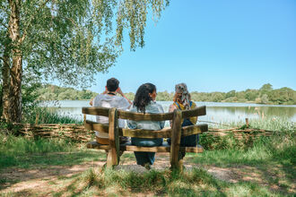 Friends sat on a natural wood bench overlooking a wildlife lake
