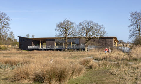 A view over the fen at Carlton Marshes towards the Visitor Centre, with a family walking along a footpath.