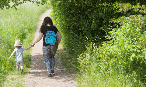 a mother and child walking hand in hand away from the camera along a path surrounded with greenery