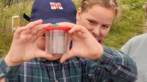 Young boy holding up a baby toad in a bug pot. 