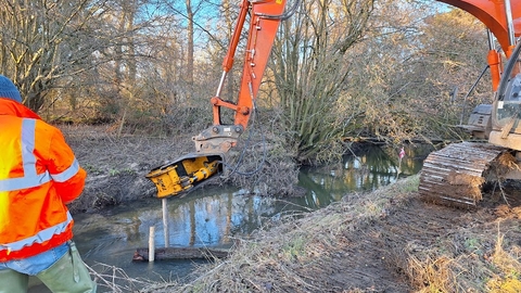 A digger placing a log flow deflector in the river channel.
