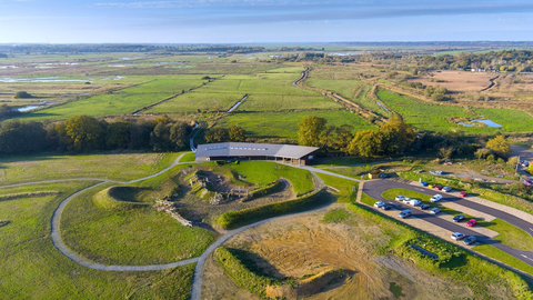 A contemporary visitor centre building sits within the vast green landscape of marshes and wildlife habitat.