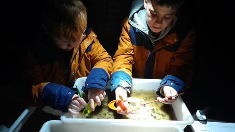 Two children leaning over a white tray lit by a torch