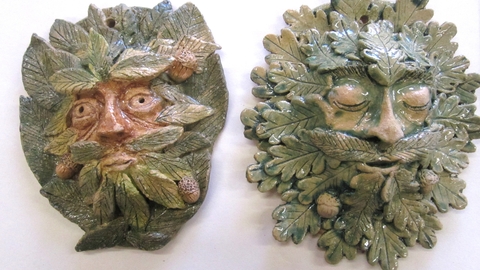 two clay green man faces by artist Phil Stearn. One has open eyes and pointed leaves, one has closed eyes and oak leaves.