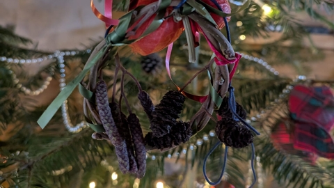 Willow and cone christmas decoration hanging on a fir tree with lights in the background