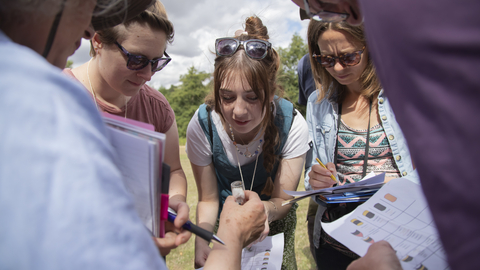 People holding paper looking at an insect