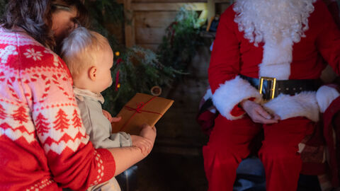 A child at Santa's grotto sitting on an adults lap holding a present