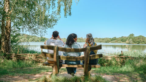 Friends sat on a natural wood bench overlooking a wildlife lake