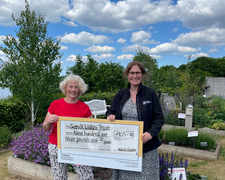Two people holding a giant check outside, looking at the camera and smiling