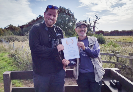 Jamie and Les holding a certificate between them and smiling at the camera 