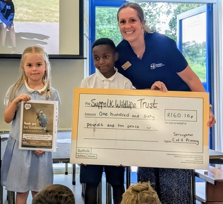 Gina with two primary children holding a certificate and giant cheque 