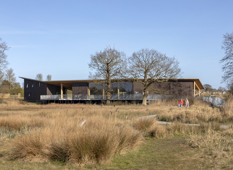 A view over the fen at Carlton Marshes towards the Visitor Centre, with a family walking along a footpath.