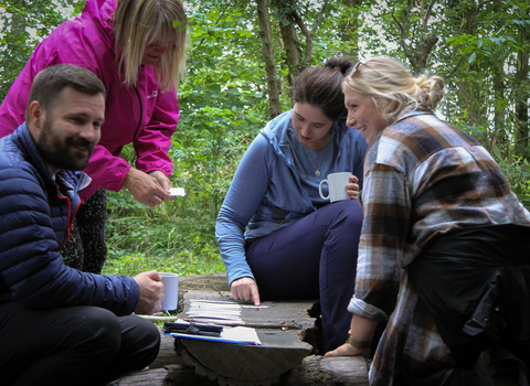 Four people gathered around a low wood table in the woods