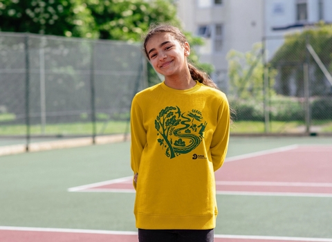 A young girl standing on a tennis court wearing a bright yellow jumper