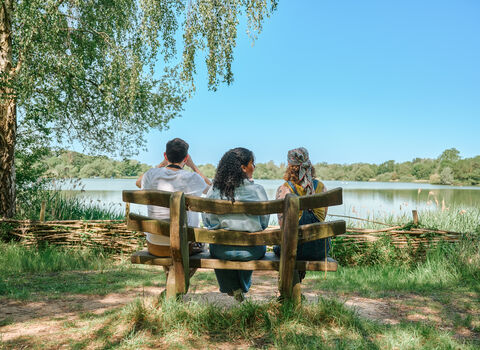 Friends sat on a natural wood bench overlooking a wildlife lake